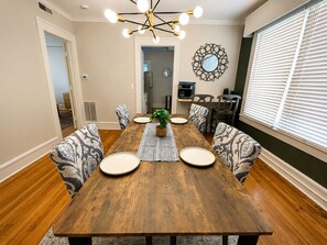Comedor con mesa de madera, sillas estampadas, una planta central y un adorno en la pared.