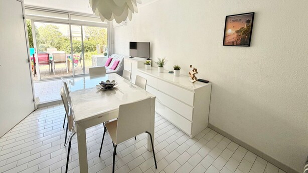 A modern, well-lit room with a dining table, chairs, a TV, and a large window. - Apartment with AC near beaches - 5 guests (Le Grau-du-Roi)