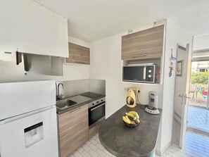A compact kitchen with a microwave, oven, sink, and a fruit bowl on the counter. - Apartment with AC near beaches - 5 guests (Le Grau-du-Roi)