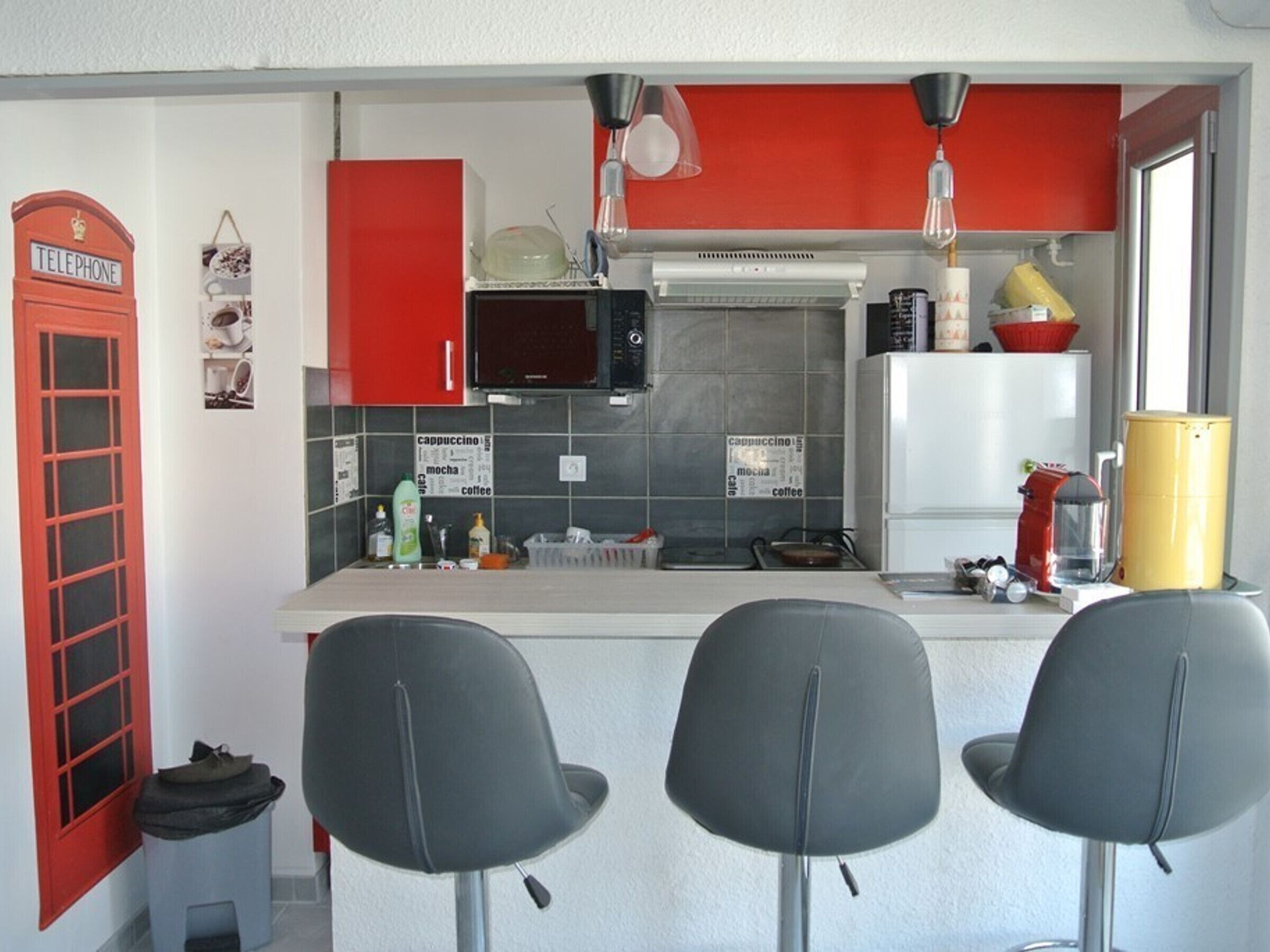 Eine kompakte Küche mit einer roten Telefonzelle, einer Mikrowelle, einer Kaffeemaschine und einer kleinen Bar mit zwei Stühlen.