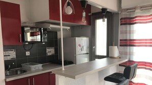 Eine kleine Küche mit Kühlschrank, Kaffeemaschine und Spüle. Zwei Barhocker und ein Fenster mit Vorhängen.