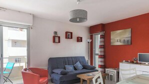 Ein modernes Wohnzimmer mit einer Couch, einem roten Sessel, einem Glastisch und einem Fernseher.