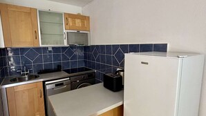 Een kleine keuken met een magnetron, fornuis, vaatwasser en een witte koelkast.
