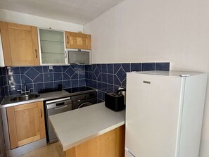 Eine kompakte Küche mit Mikrowelle, Herd, Geschirrspüler und einem weißen Kühlschrank.