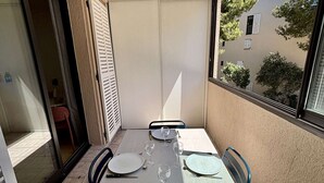 Een balkon met een tafel gedekt voor twee personen, een schuifdeur en uitzicht op gebouwen en bomen.