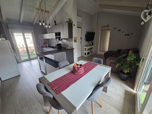 Een moderne keuken met een eethoek, een televisie en een woonkamer met een bank en planten.