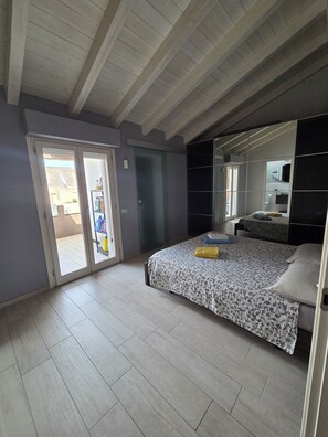 A bedroom with a bed, a wardrobe, a sliding glass door, and a ceiling with wooden beams. - Casa ReGa - Central Penthouse with Private Parking in Quartu (Quartu Sant'Elena)