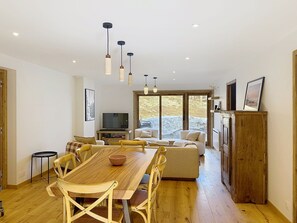 Un espacio de estar moderno con una mesa de comedor de madera, sofás, un televisor y un ventanal grande.