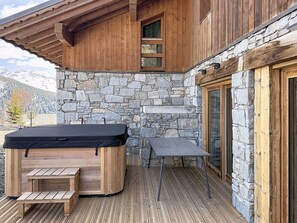 A wooden deck with a hot tub, a table, and a stone wall. - Elegant apartment mountain view - 8 guests (Montvalezan-La Rosière)
