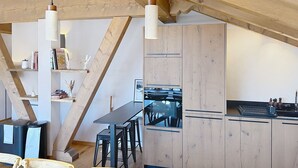 Moderni keittiö, jossa on puupalkkeja, ruokailutila tuoleineen ja musta työtaso.