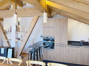 A modern kitchen with wooden beams, a dining area with chairs, and a black countertop. - Apartment with mountain view - 12 guests (Montvalezan-La Rosière)