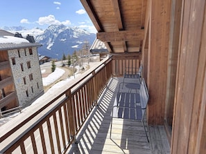 A wooden balcony with a view of snow-covered mountains and a stone building. - Apartment with mountain view - 12 guests (Montvalezan-La Rosière)