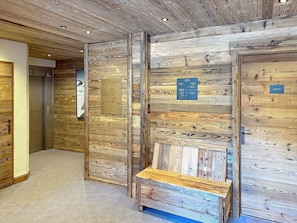 A hallway with wooden panel walls, a bench, and directional signs. - Apartment with mountain view - 12 guests (Montvalezan-La Rosière)