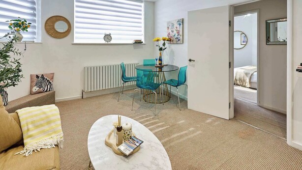A modern living room with a round glass table, a sofa, a coffee table, a radiator, a window with blinds, and a door leading to another room. - Boutique One Bed Apartment in Kemp Town (Brighton and Hove)