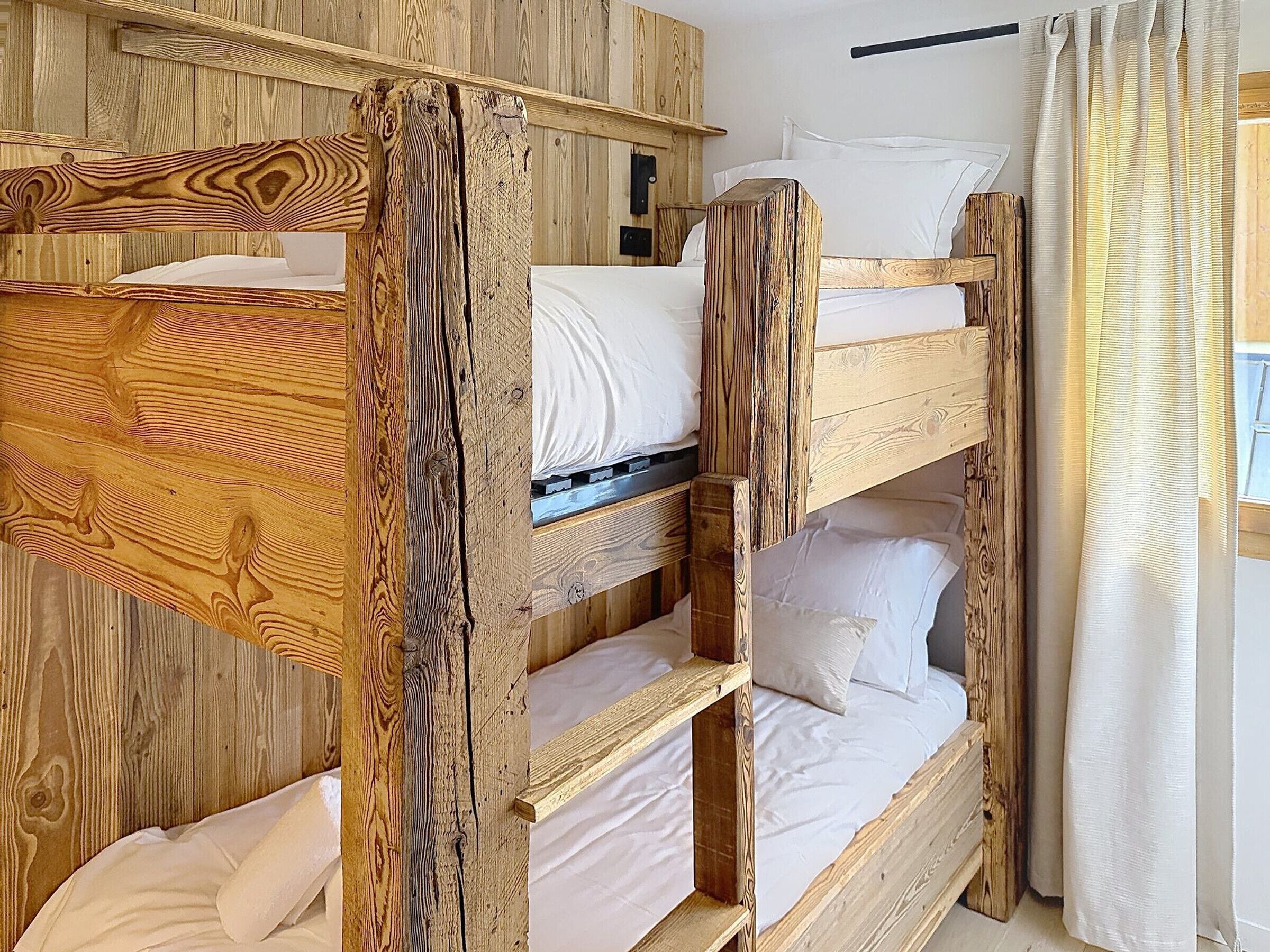 A bunk bed room with wooden walls and a window with curtains.