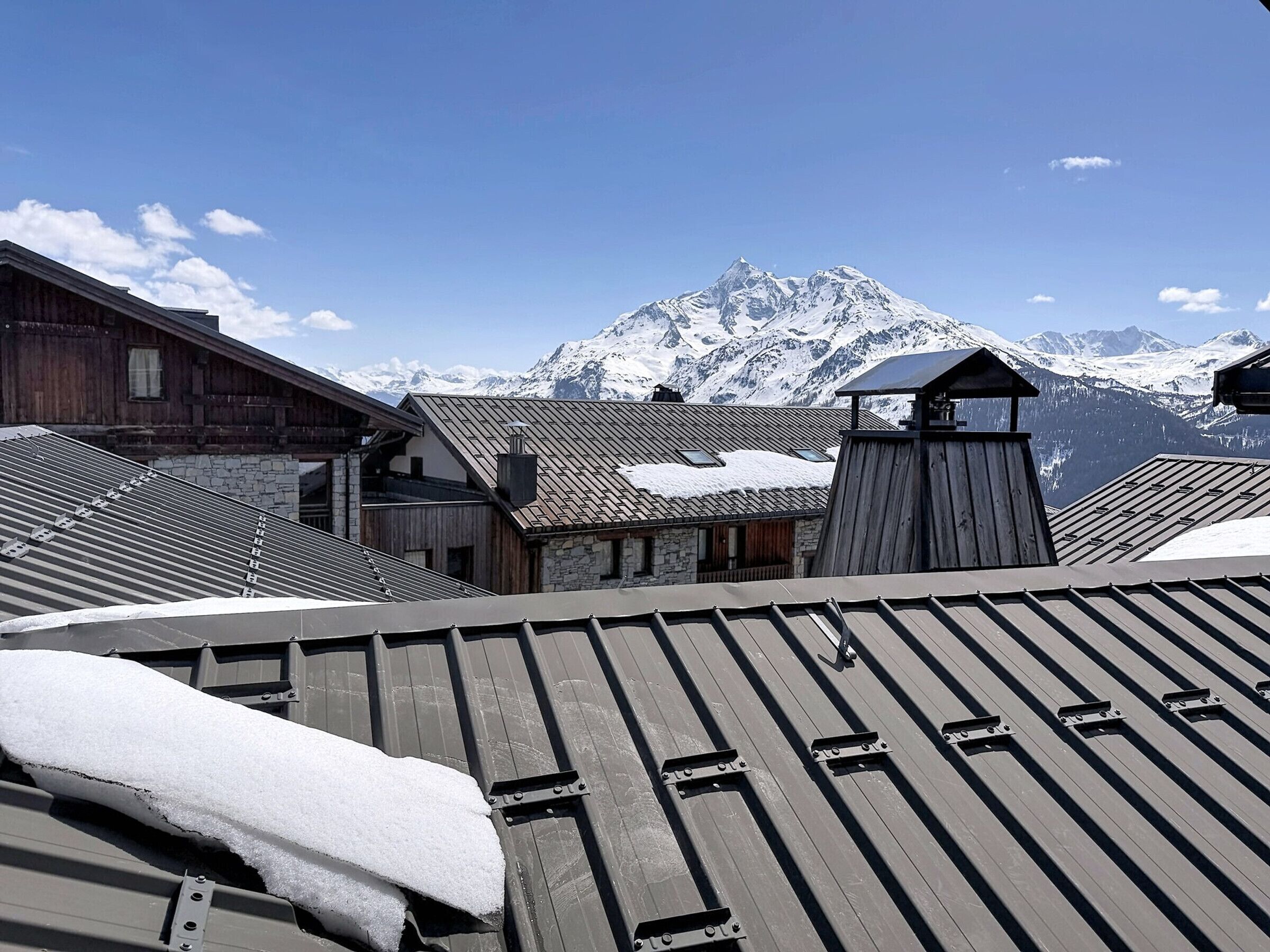 A mountain cabin with a metal roof, stone walls, and a wooden structure with a chimney.