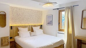 Un dormitorio con cama de madera, cabecera con panel moteado, mesita de noche, espejo y ventana con cortinas.