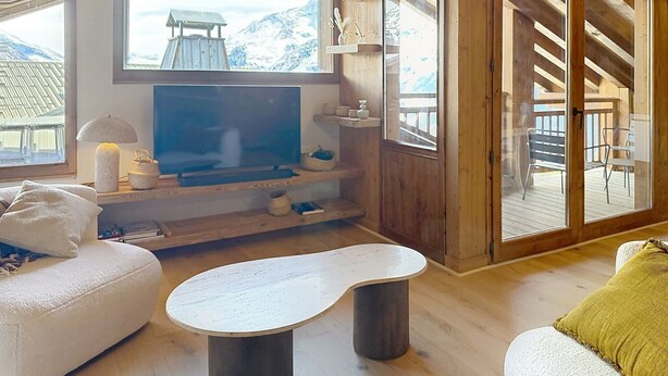 Una habitación acogedora con televisión, muebles de madera y vistas a las montañas a través de amplios ventanales.