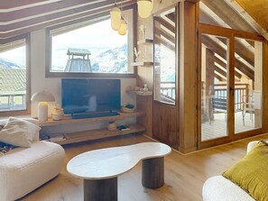 A cozy room with a television, wooden furniture, and a view of mountains through large windows. - Apartment with mountain view - 10 guests (Montvalezan-La Rosière)