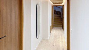 Un pasillo con piso de madera, paredes blancas y techo de madera con iluminación empotrada.