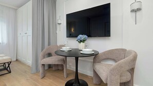 A modern dining area with two chairs, a round table, a flat-screen TV, and a wall-mounted light fixture.