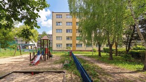 A playground with a slide and sandpit, surrounded by trees and a building in the background.