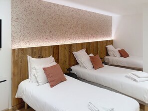Ein Hotelzimmer mit zwei Einzelbetten, einem Holzkopfstück, weißer Bettwäsche und einer gesprenkelten Decke.