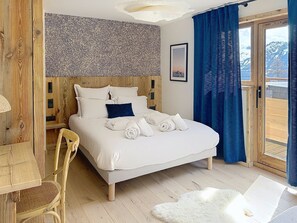 A bedroom with a bed, a chair, a wooden wall, a window, and a door. - Alpine apartment, mountain view - 9 guests (Montvalezan-La Rosière)