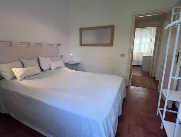 A bedroom with a large bed, a bedside table with a lamp, a mirror on the wall, and a wardrobe.