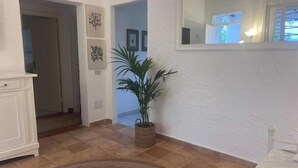 Een gang met een potplant, een vloerkleed en afbeeldingen in lijsten aan de muur.