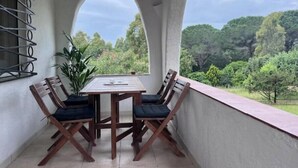 Een balkon met een tafel, stoelen, een bloempot en uitzicht op een bebost landschap.
