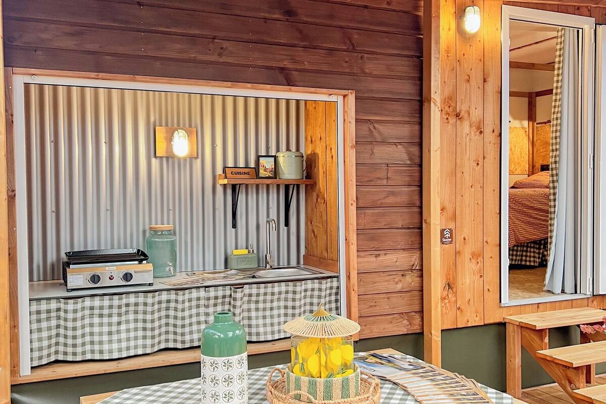 Una cabaña de madera con mesa, sillas, zona de cocina y un espejo.