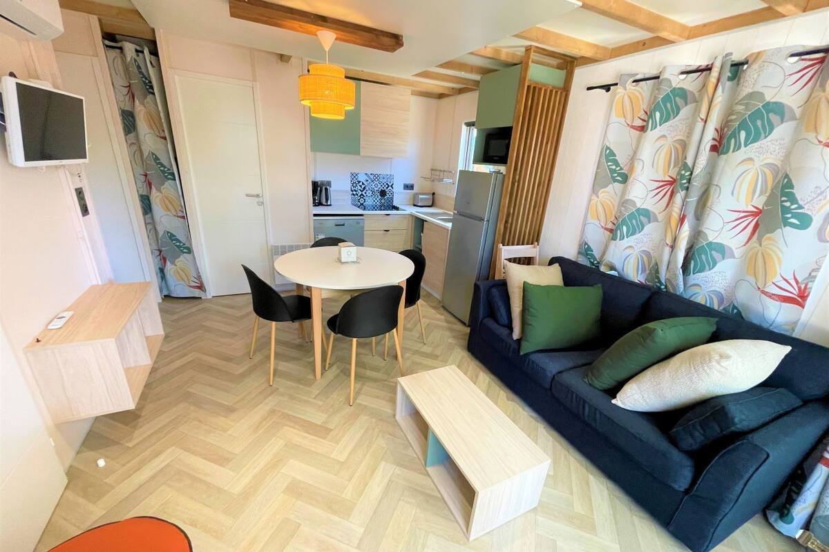 Un espacio habitable compacto con comedor, sofá y cocina al fondo.