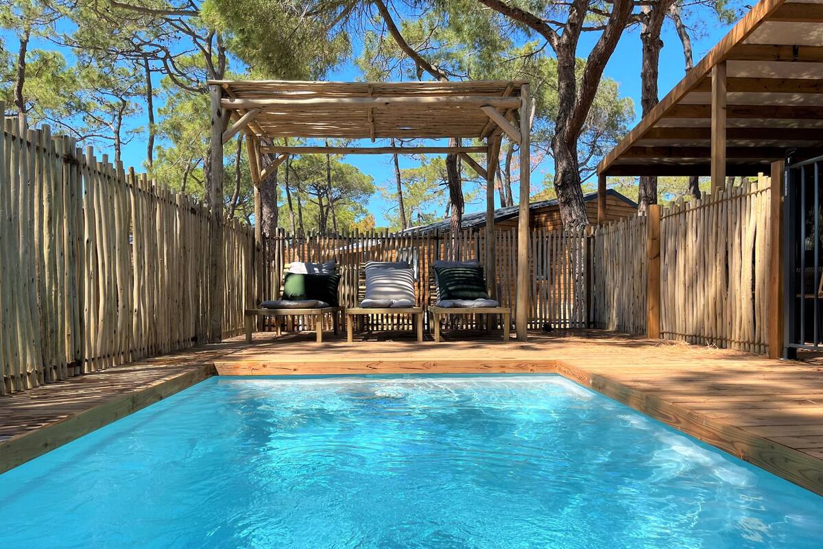 Una terraza de madera con piscina, sillas de descanso y una pérgola.