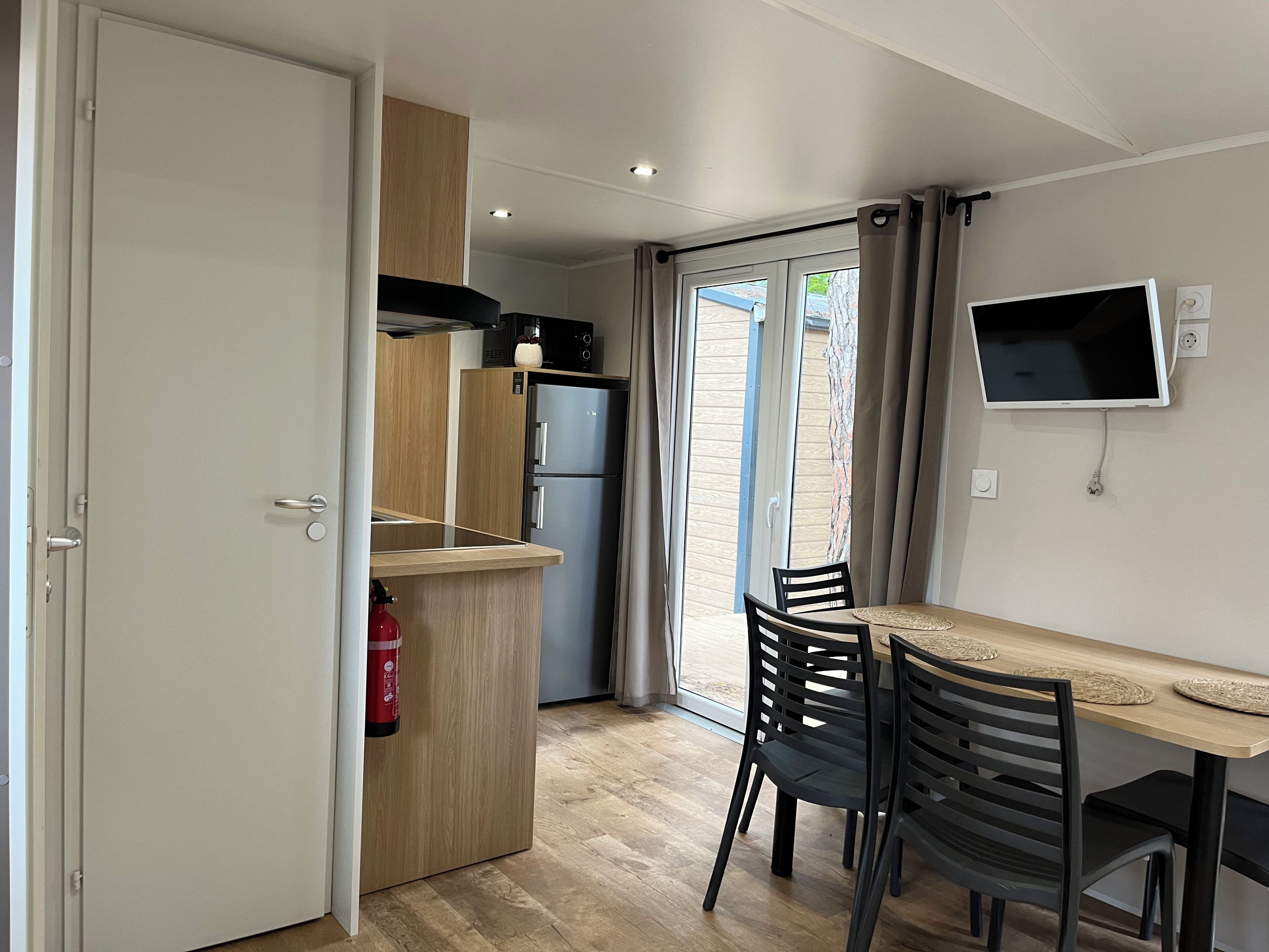 Eine kleine Küche mit Kühlschrank, Holzschränken und einem Essbereich mit Tisch und Stühlen.