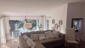 Sala de estar com sofá, poltrona, mesa e vista para uma piscina.