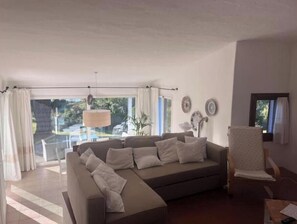 Ein Wohnzimmer mit einer Couch, einem Sessel, einem Tisch und Blick auf einen Pool.