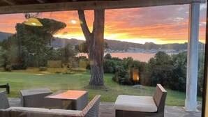 Uma área externa com mobiliário de vime e vista para o pôr do sol sobre a água.