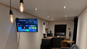 Een slaapkamer met een bed, een grijze bank, een televisie waarop een film draait en een kitchenette op de achtergrond.