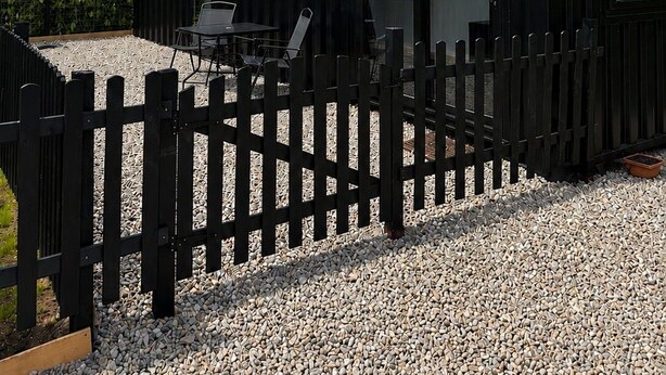 Een moderne, zwarte metalen constructie met een glazen deur, een klein terras en een grindpad.