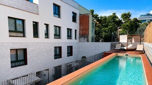 Une piscine rectangulaire bordée de carreaux, entourée d’un bâtiment blanc doté de nombreuses fenêtres et d’une partie en briques.