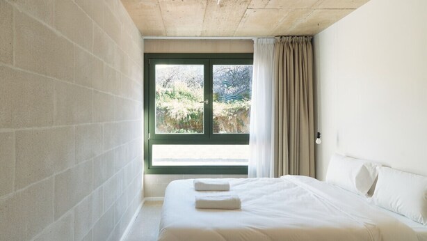 Une chambre avec un grand lit, une fenêtre avec des rideaux et une vue sur la verdure.