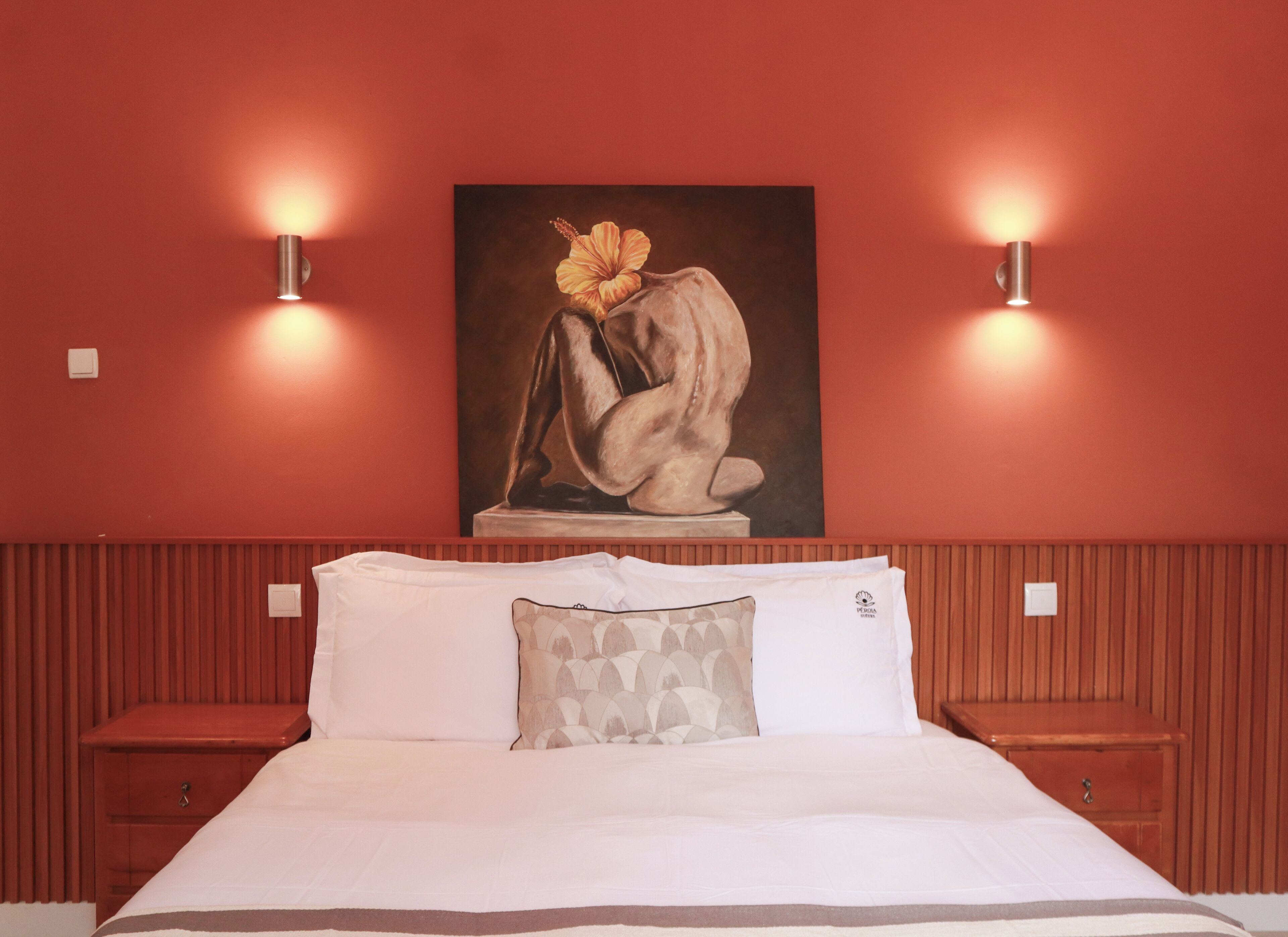 Una habitación de hotel con cama, dos mesitas de noche, un cuadro colgado en la pared y dos apliques.
