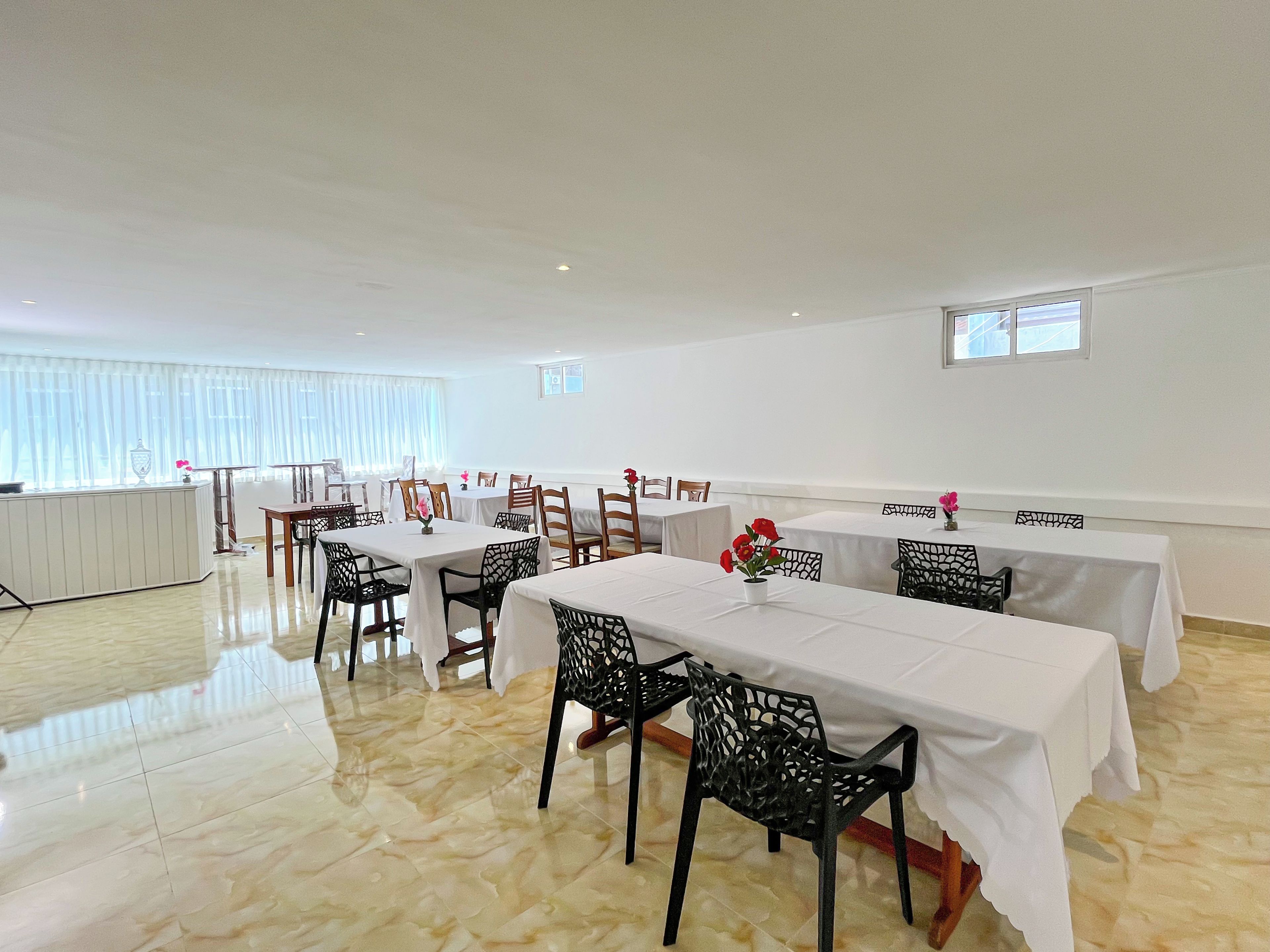 A dining area with tables and chairs, a radiator, and a window with blinds.