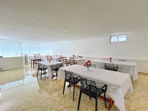 A dining area with tables and chairs, a radiator, and a window with blinds.