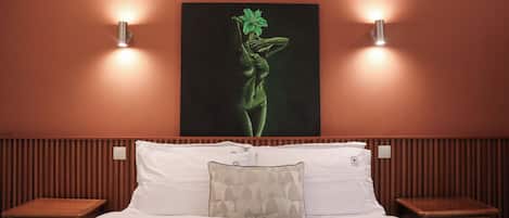 Une chambre d’hôtel comprenant un lit, deux tables de chevet, une œuvre d’art accrochée au mur et deux appliques murales.