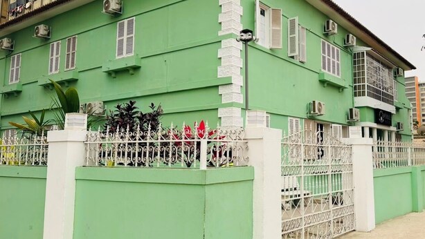 A green building with white window shutters, a white fence, and air conditioning units. - Pérola Suítes Boutique Hotel (Luanda)