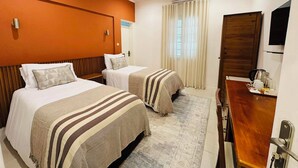 A hotel room with two beds, a wooden headboard, a desk with a kettle, and a television. - Pérola Suítes Boutique Hotel (Luanda)