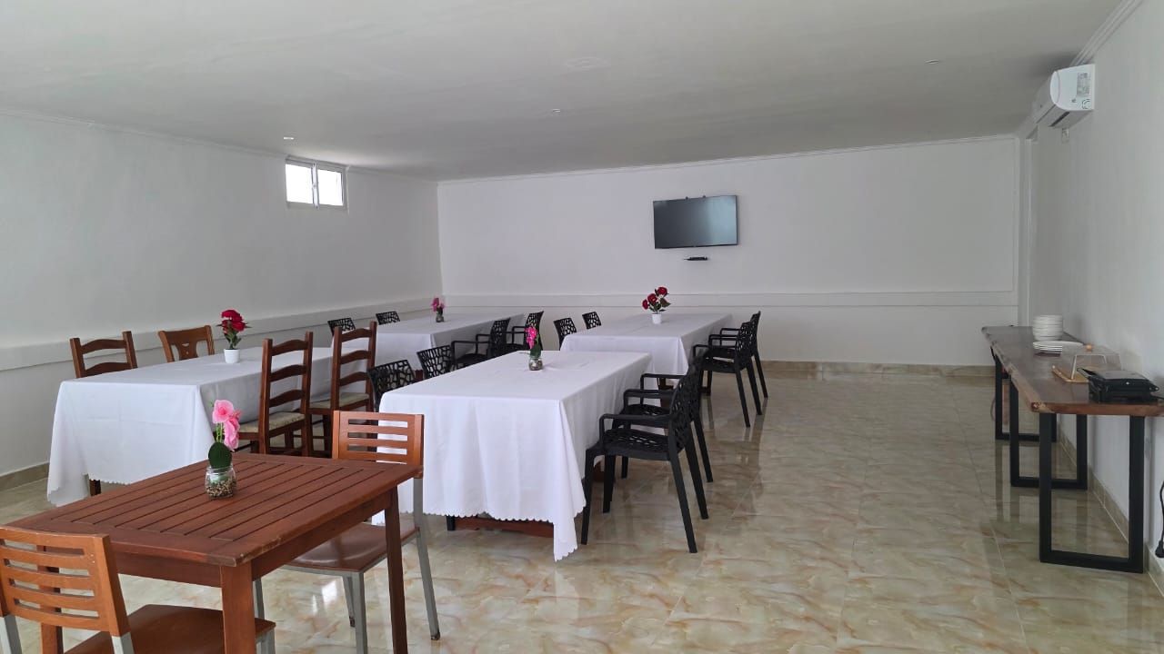 A spacious room with multiple tables and chairs, a flat-screen TV mounted on the wall, and a tiled floor.