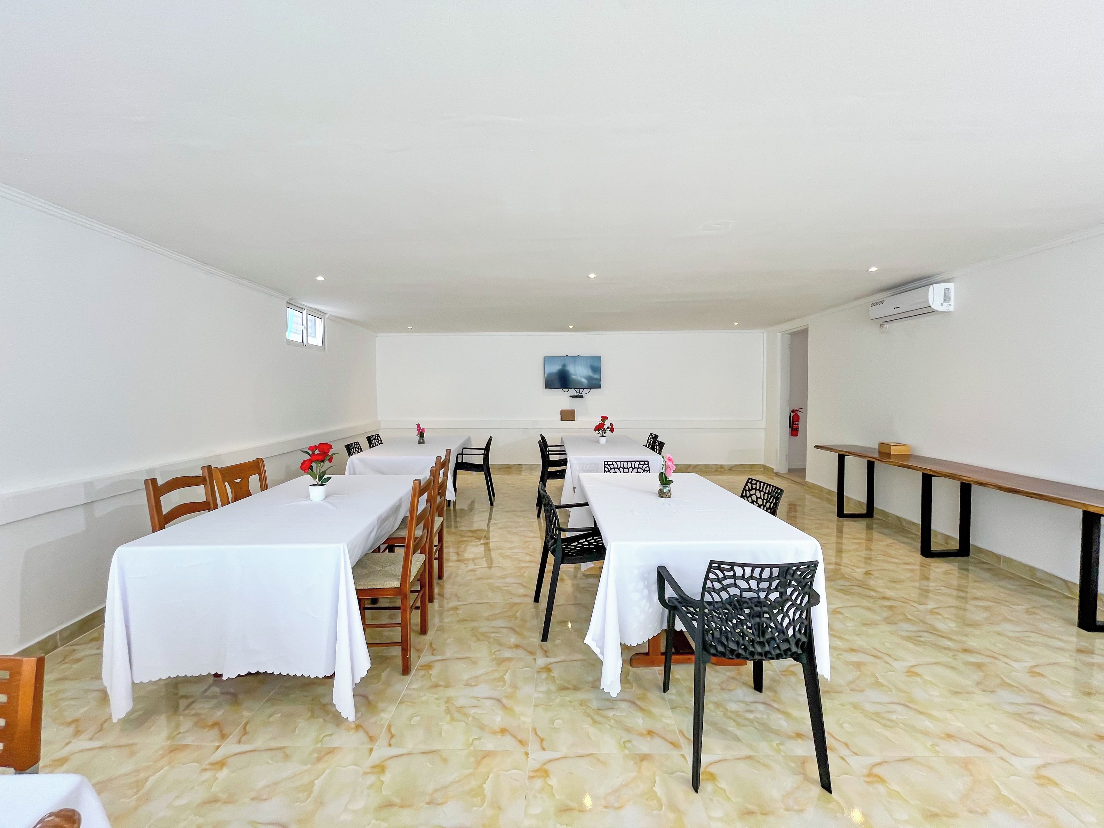 A conference room with white tables, chairs, and a flat-screen TV on the wall.